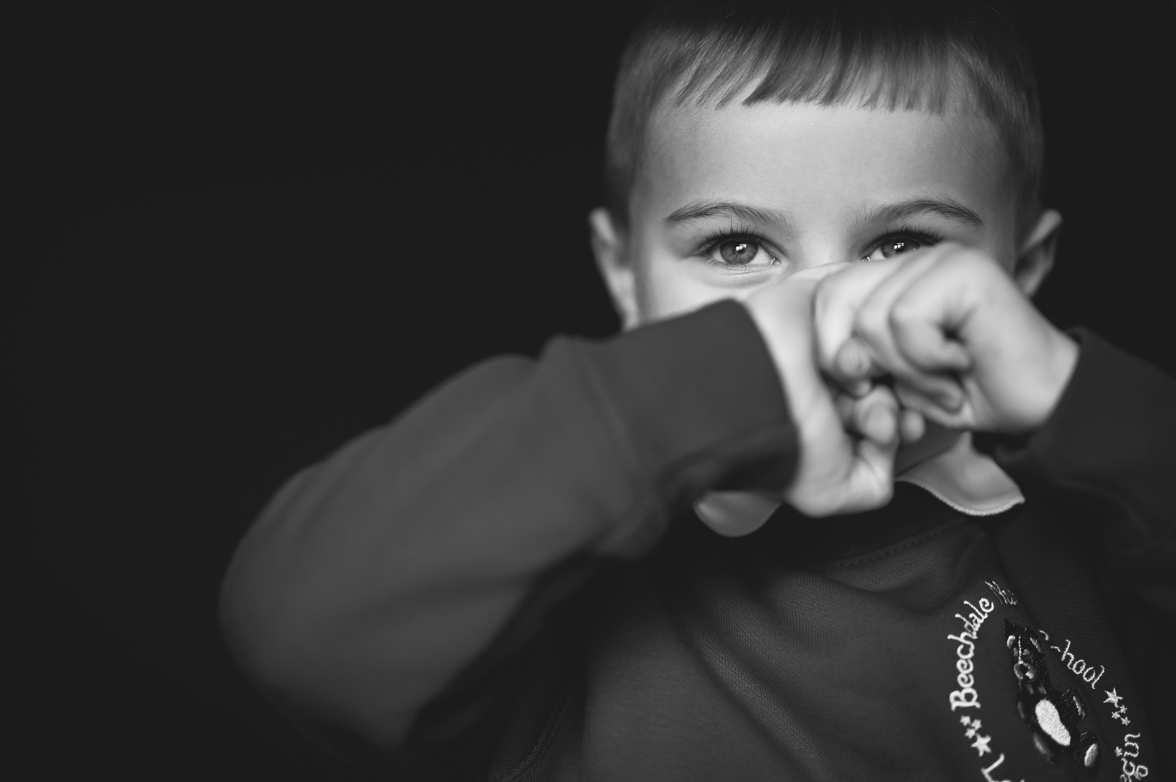 Fine art portrait of boy hiding playfully behind hands